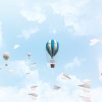 shutterstock 1117048970 colorful balloons flying among paper planes and against a cloudy blue sky